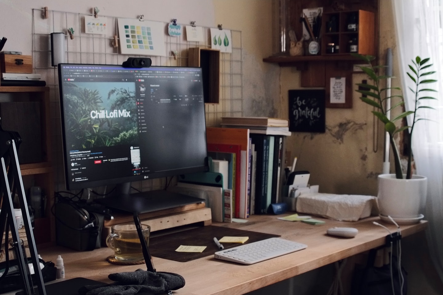 A desk with a computer, tea, and a potted plant.