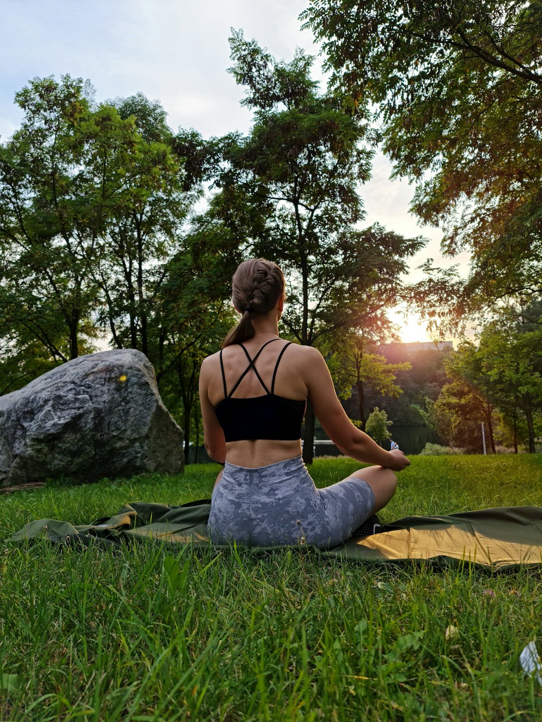 Woman sits on a yoga mat in a park.